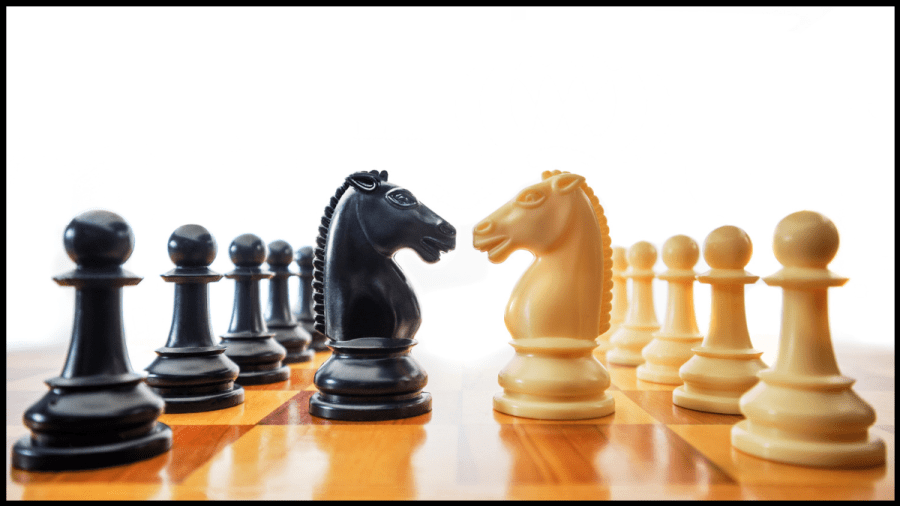 Photo of a chess board with the black and white knights facing off and a line of pawns behind each of them