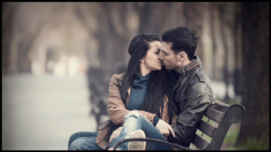 Photo of a young couple kissing on a park bench