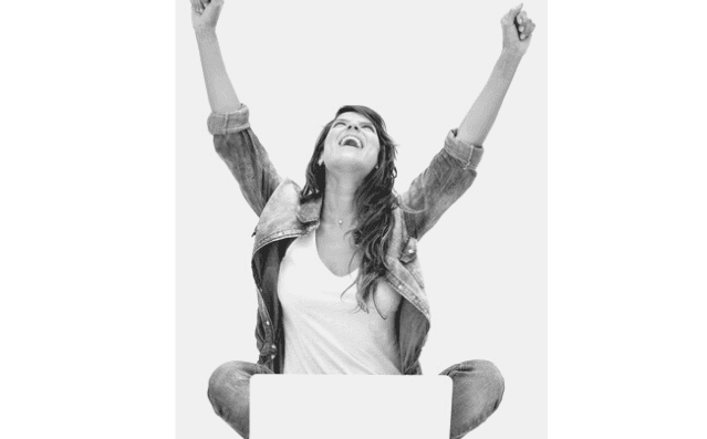 Featured Images - Woman sat cross legged before a laptop, arms raised laughing. Image from Depositphotos