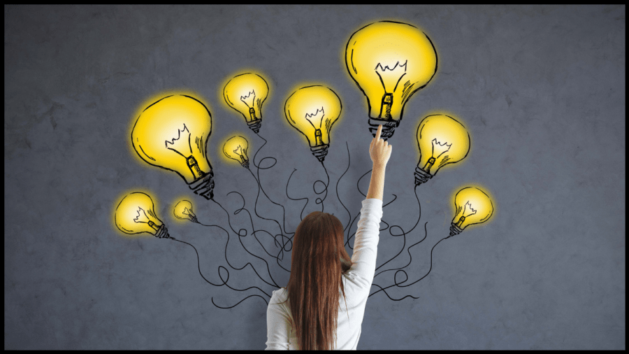Image of multiple glowing light bulbs drawn on a dark wall, with a woman in front reaching up to point at one.