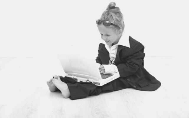 Featured Images - Photo of a little girl, dressed in a business suit, sunglasses and working on a laptop. Image bought from DepositPhotos