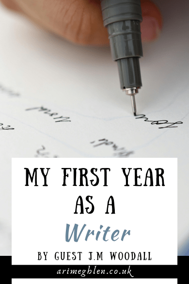 Close up of a fine-tipped black pen held by fingers, and writing on lined paper. Text overlay reads My First Year As A Writer by Guest JM Woodall