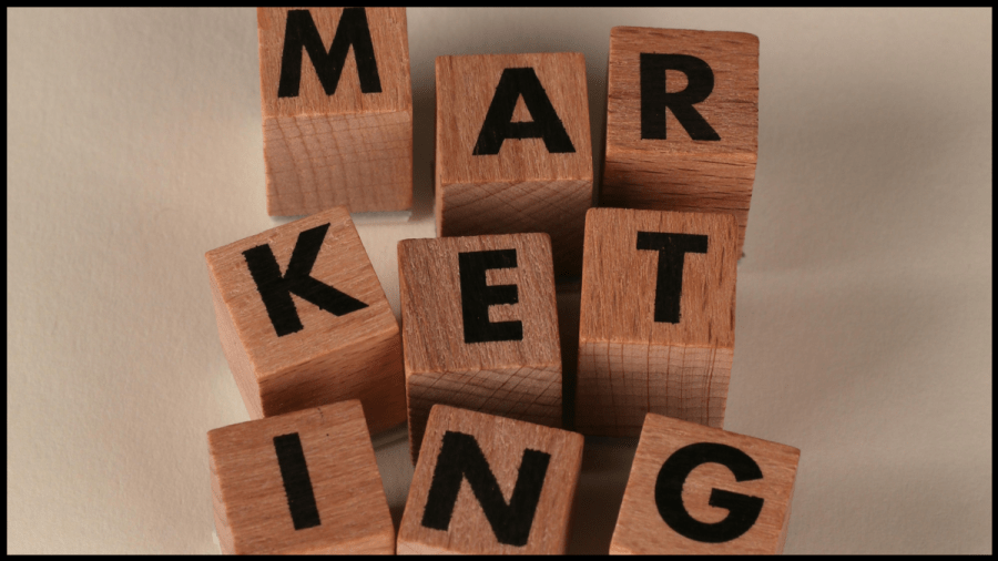 Photo of brown wooden cubes each with a letter written in black. They spell out the word Marketing.