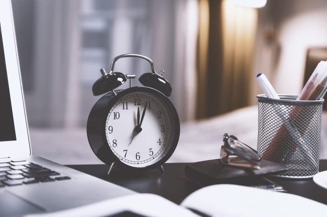 Time management. Image of alarm clock on a desk beside a laptop