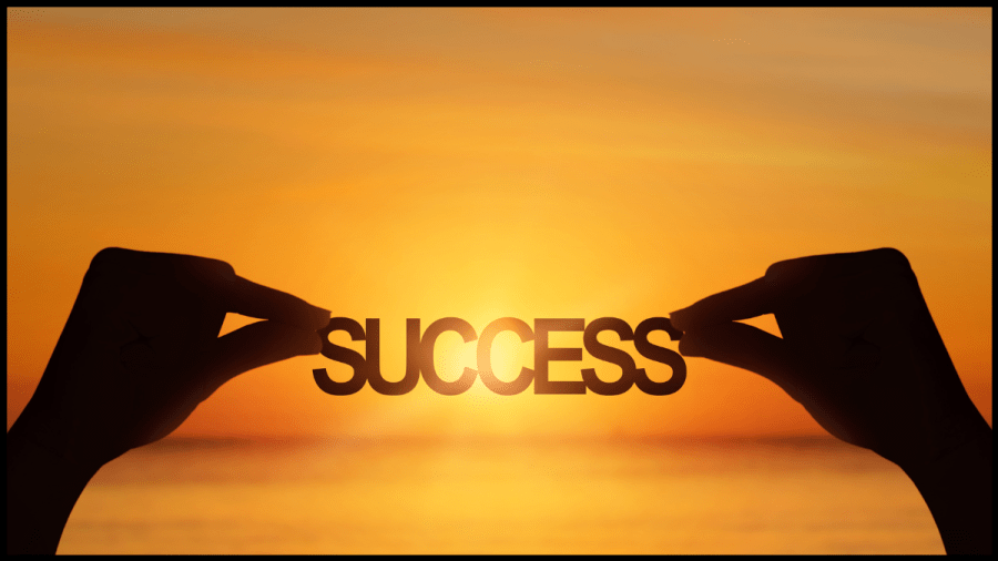 The word Success held between two hands with a sunrise behind it.