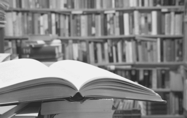 Featured Image - book open on a pile of books with bookshelves in the background. Library. Image from Pixabay