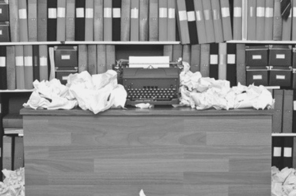 Featured Images - Messy desk with piles of scrunched up papers and typewriter