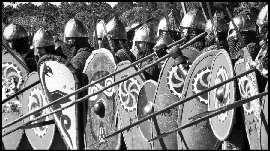 Black and white photo of men in chainmail, helmets and holding shields and spears.