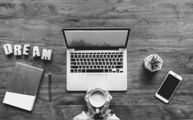 Featured Images - Laptop on a desk surrounded by a notepad, pen, phone and plant. Person sat before laptop holding a cup of coffee. image from pixabay