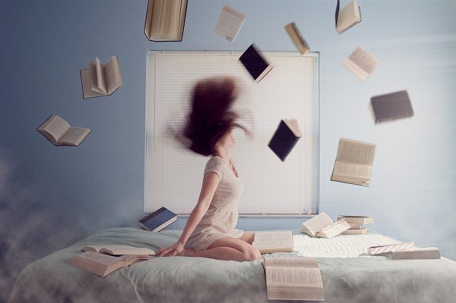 Woman sat on bed surrounded by flying books. Image of Pixabay