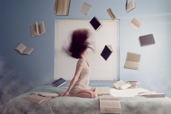 Woman sat on bed surrounded by flying books.  Image of Pixabay