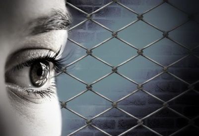 Woman imprisoned. Day of the Imprisoned Writer. Close up of a woman's eye with prison fencing behind.