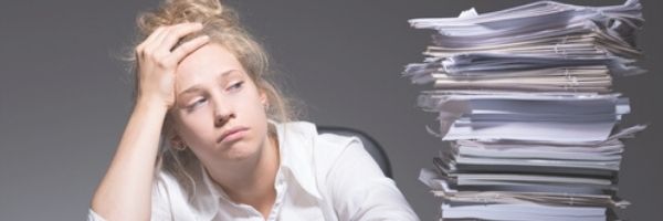 Stressed Woman staring at a large towering stack of papers in an in-tray. Image purchased from DepositPhotos
