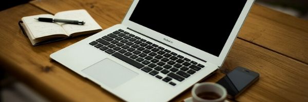 Laptop on desk beside an open notebook, pen, coffee cup and phone.  Image from Pixabay