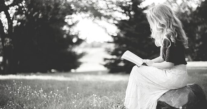Featured Image - Woman sitting on a rock in a field reading a book. Image from Pixabay