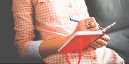 Woman in a checked shirt writing in a journal. Image from Pixabay
