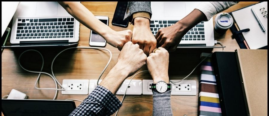 Image of hands all fist bumping above a desk. Teamwork