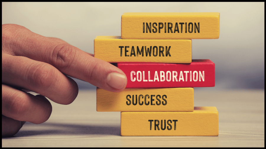 Photo of yellow coloured wooden blocks with words on them and in the centre a red block with collaboration written on it and a hand pulling out the red block. Image from Canva
