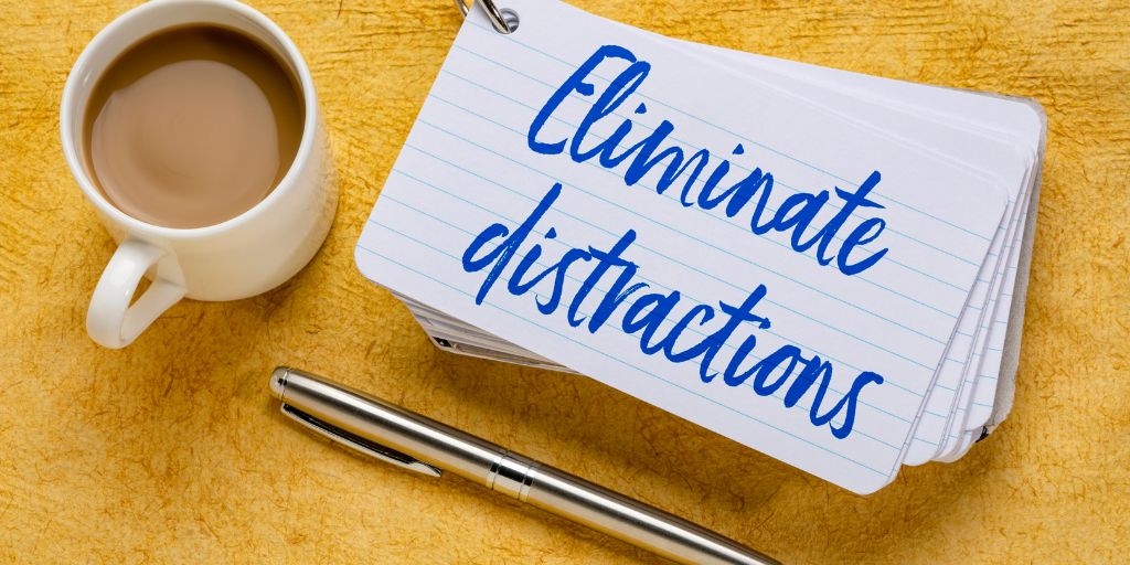 Photo of a stack of index cards with the words Eliminate distractions written across the top. A coffee cup and pen sit beside the cards.