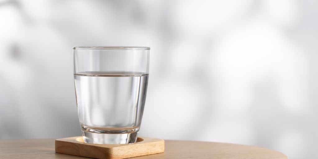 Photo of a glass of water on a wooden coaster on a table. Image from Canva
