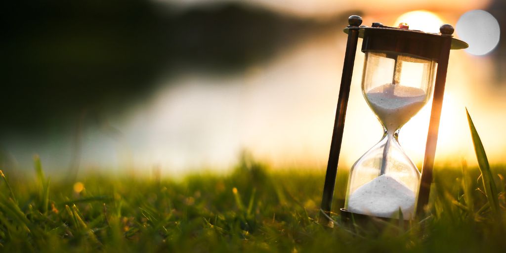 Photo of an hourglass sitting in the glass with sand in both the top and bottom. Image from Canva