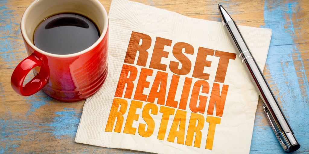 Photo of a red coffee cup full of coffee, sat on the edge of a napkin that has text that reads Reset Realigm Restart.